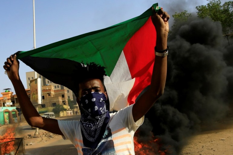 A protester carries a Sudanese national flag as he burns tyres during a demonstration against a report of the Attorney-General on the dissolution of the sit-in protest in Khartoum