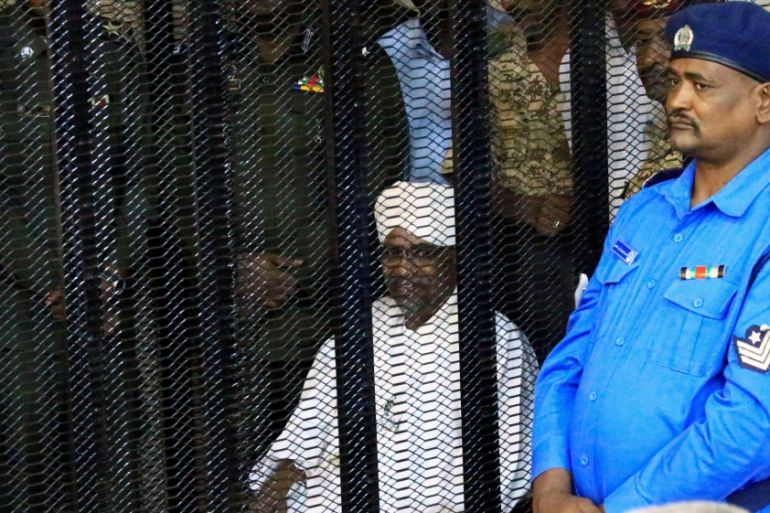 Sudan''s former president Omar Hassan al-Bashir sits guarded inside a cage at the courthouse where he is facing corruption charges, in Khartoum
