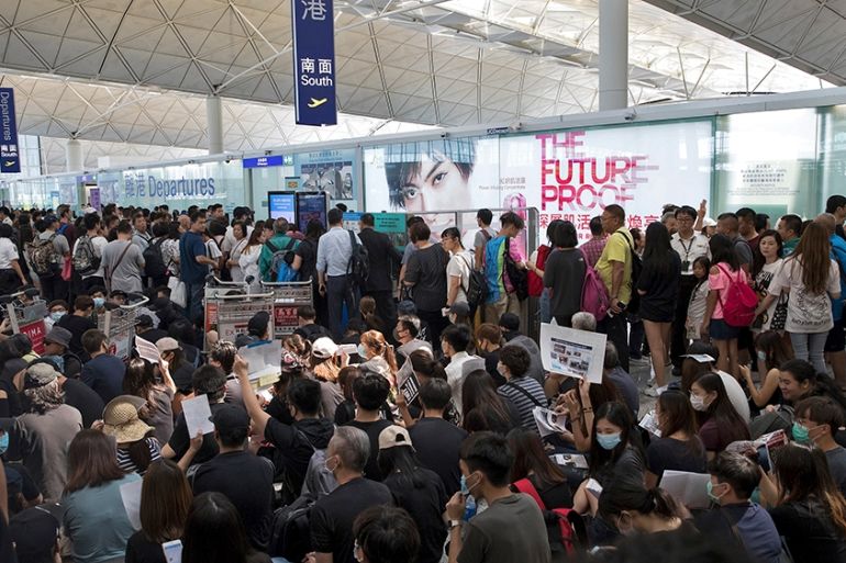 Traveller look at protesters hold placards and posters take part in a sit-in rally near the departure gate of the Hong Kong International airport in Hong Kong, Tuesday, Aug. 13, 2019. Some flights sta