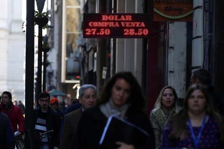 Pedestrians walk past an electronic board showing currency exchange rates in Buenos Aires'' financial district, Argentina