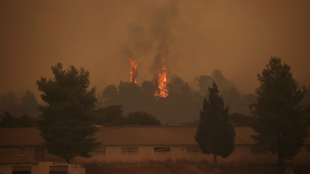  Flames rise behind a farm as a wildfire burns near the village of Psachna, on the island of Evia