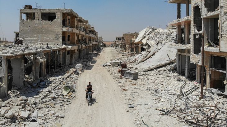 An aerial view taken on August 3, 2019, shows Syrian men riding a motorcycle past the rubble of destroyed buildings in the town of Khan Sheikhun in the southern countryside of Idlib.