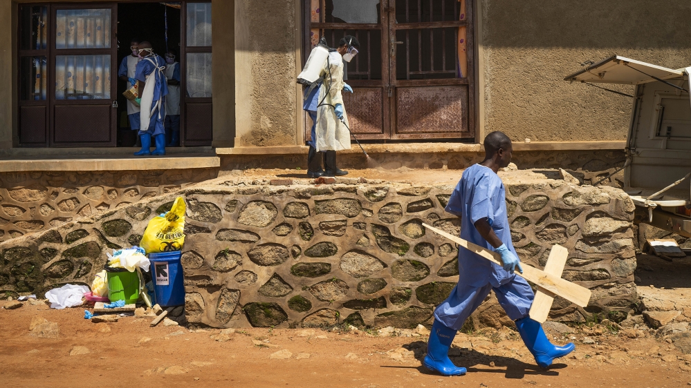 A morgue employee walks with a cross past others disinfecting the entrance to the morgue in Beni, Congo DRC [File:Jerome Delay/AP Photo]
