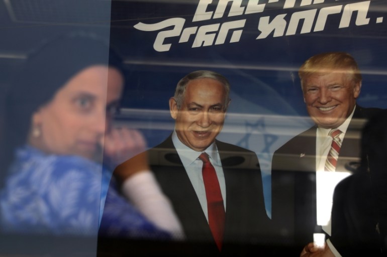 An ultra-orthodox Jewish woman is seen through a bus window along with a reflection of a Likud party election campaign banner depicting Israeli Prime Minister Benjamin Netanyahu and Trump