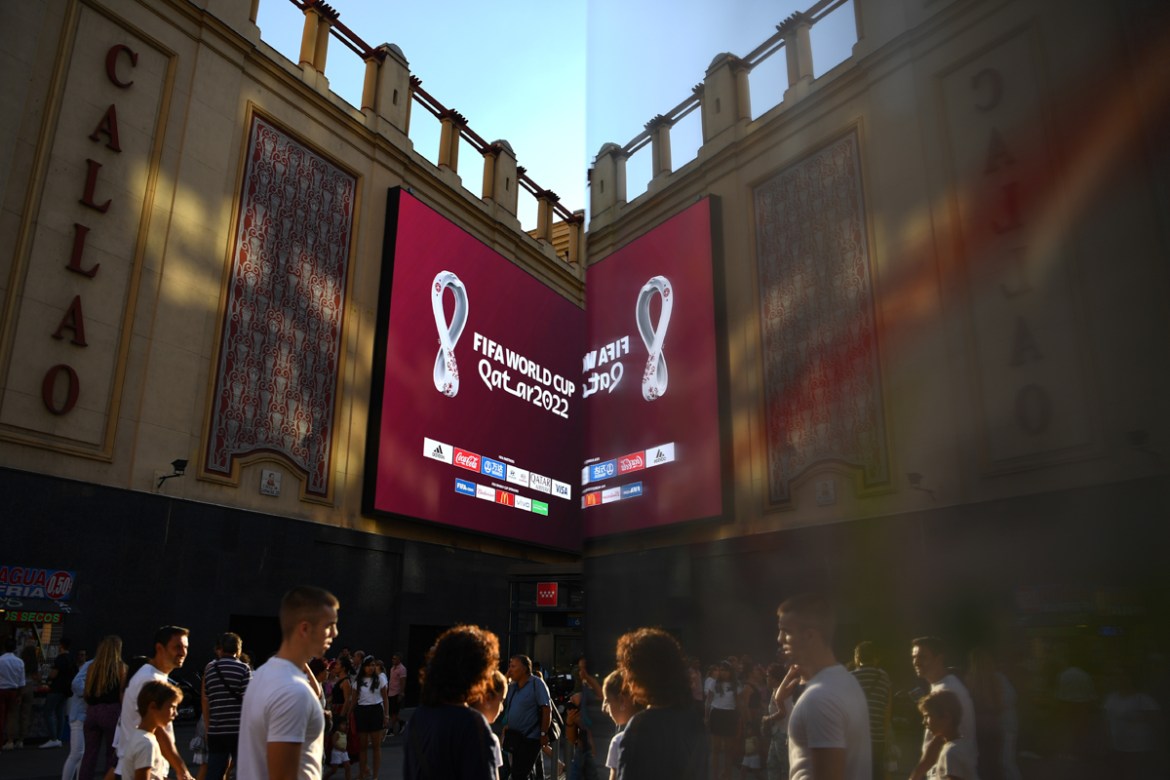 People walks by as the official logo of the FIFA World Cup Qatar 2022 is unveiled on a giant screen in Madrid on September 3, 2019. (Photo by GABRIEL BOUYS / AFP)