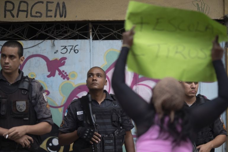 A woman holds a sign with a message that reads in Portuguese: "More school, less bullets" in front of police officers during a protest