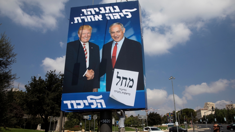 A man walks past a Likud party election campaign banner depicting Israeli Prime Minister Benjamin Netanyahu and U.S. President Donald Trump as a labourer hangs it up in Jerusalem