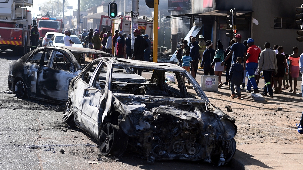 Pedestrians pass burnt out cars on the side of a street on the outskirts of Johannesburg Monday Sept. 2, 2019. Police had earlier fired rubber bullets as they struggled to stop looters who targeted bu