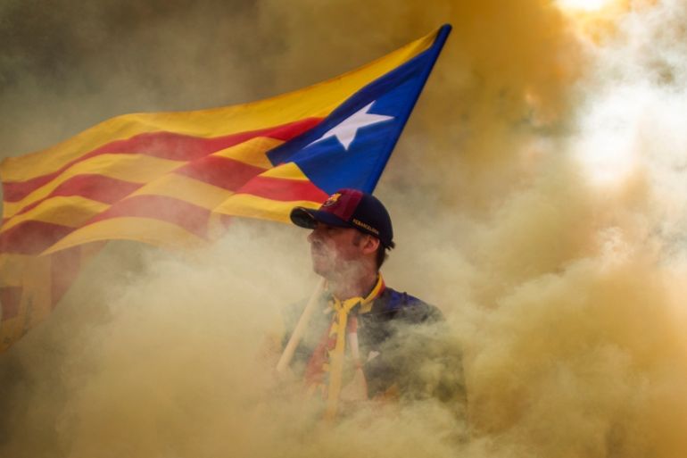 A man holding an independence flag is seen through the smoke thrown by demonstrators during the Catalan National Day in Barcelona, Spain, Wednesday, Sept. 11, 2019.