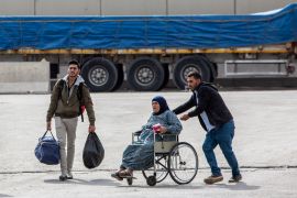A man pushes an older Syrian woman on a wheelchair while another helps with her luggage as they make their way out of the Karkamis border crossing