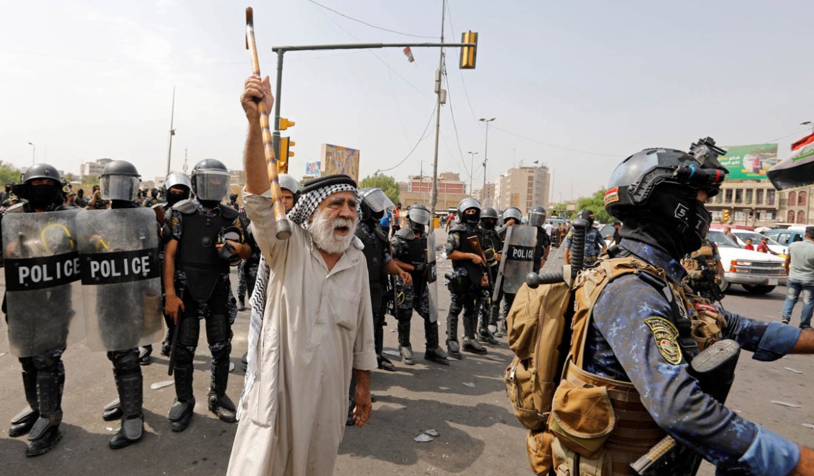 A demonstrator holds up a cane as Iraqi security forces stand guard during a protest over unemployment, corruption and poor public services, in Baghdad, Iraq October 2, 2019. REUTERS/Khalid al-Mousily