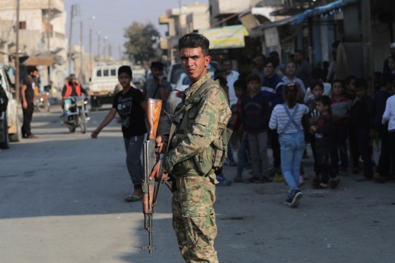A Turkey-backed Syrian rebel fighter holds a weapon as he stands along a street in the border town of Tal Abyad