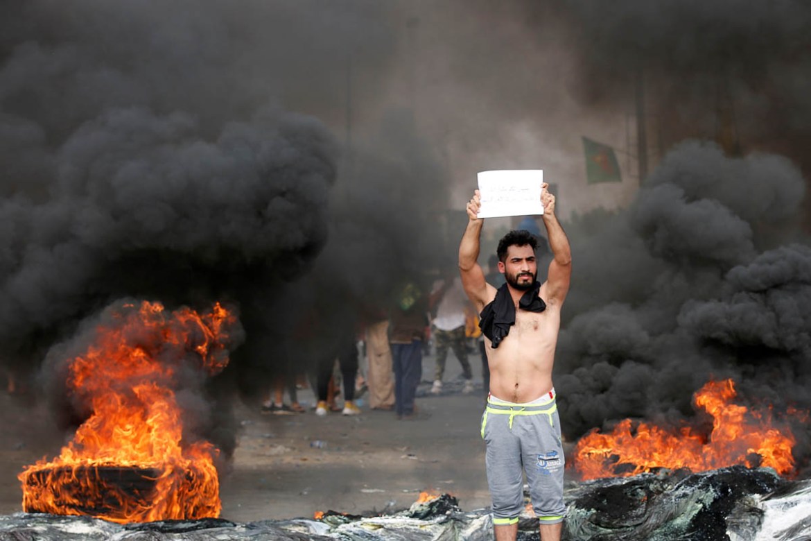 A demonstrator holds a sign as others block the road with burning tires during a protest over unemployment, corruption and poor public services, in Baghdad, Iraq October 2, 2019. REUTERS/Wissm al-Okil
