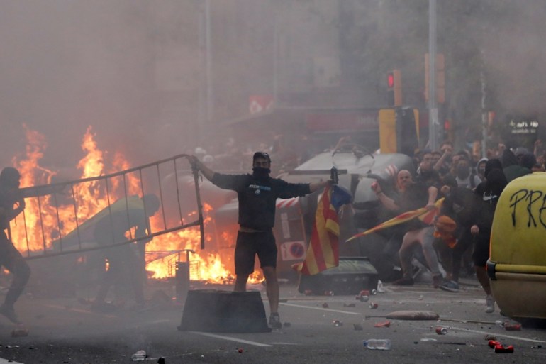 Protesters throw objects close to a burning barricade near the Police headquarters in Barcelona, on October 18, 2019, on the day that separatists have called a general strike and a mass rally.