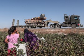Seasonal workers cut a cotton while Turkish military vehicles carrying tanks as they are on the way to Northern Syria for a military operation in Kurdish areas, near the Syrian border, near Akcakale d