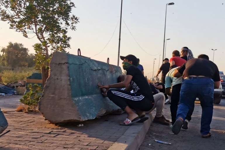 Demonstrators take cover during a protest after the lifting of the curfew, following four days of nationwide anti-government protests that turned violent, in Baghdad