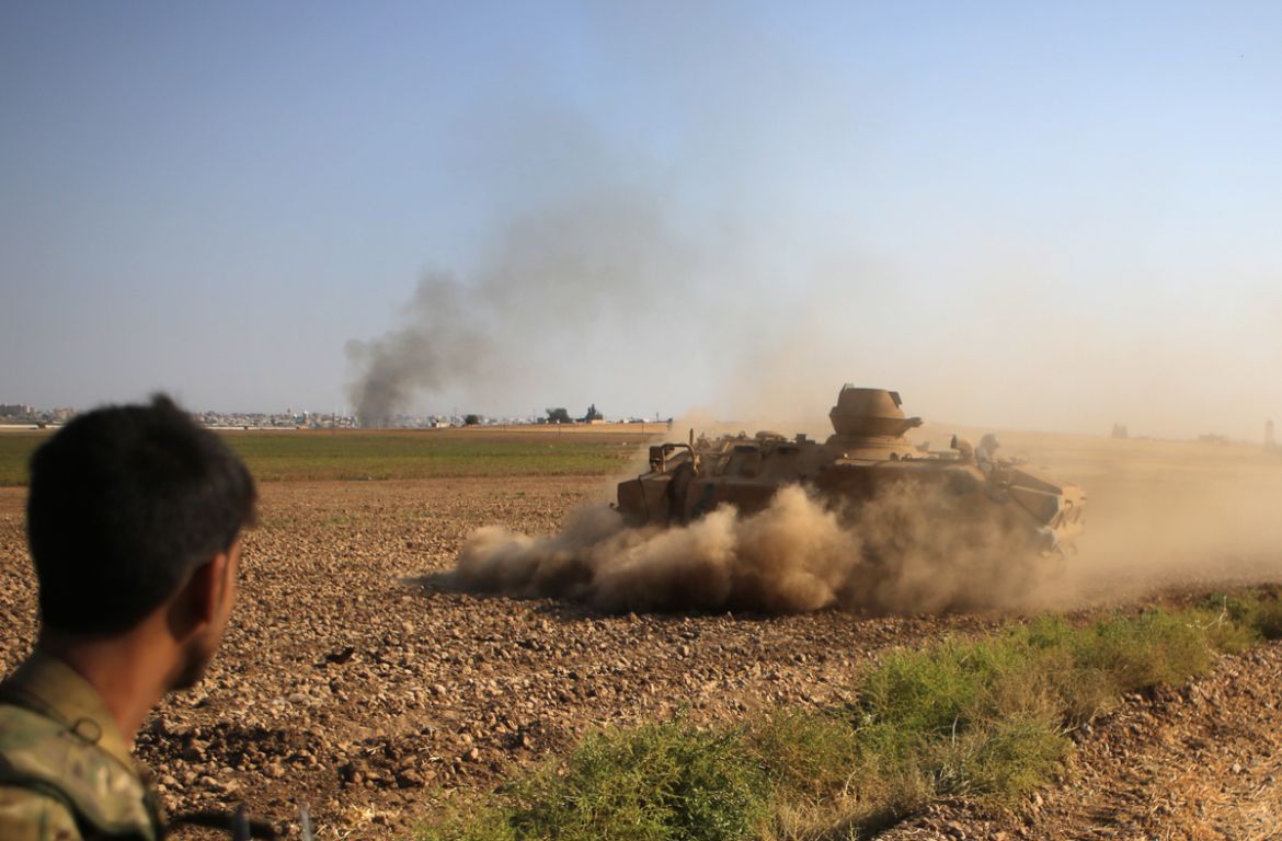A Syrian fighter with the Turkey-backed forces watches an armoured personnel carrier manoeuvring on the outskirts of the border Syrian town of Tal Abyad on October 13, 2019. - Fighting has engulfed th