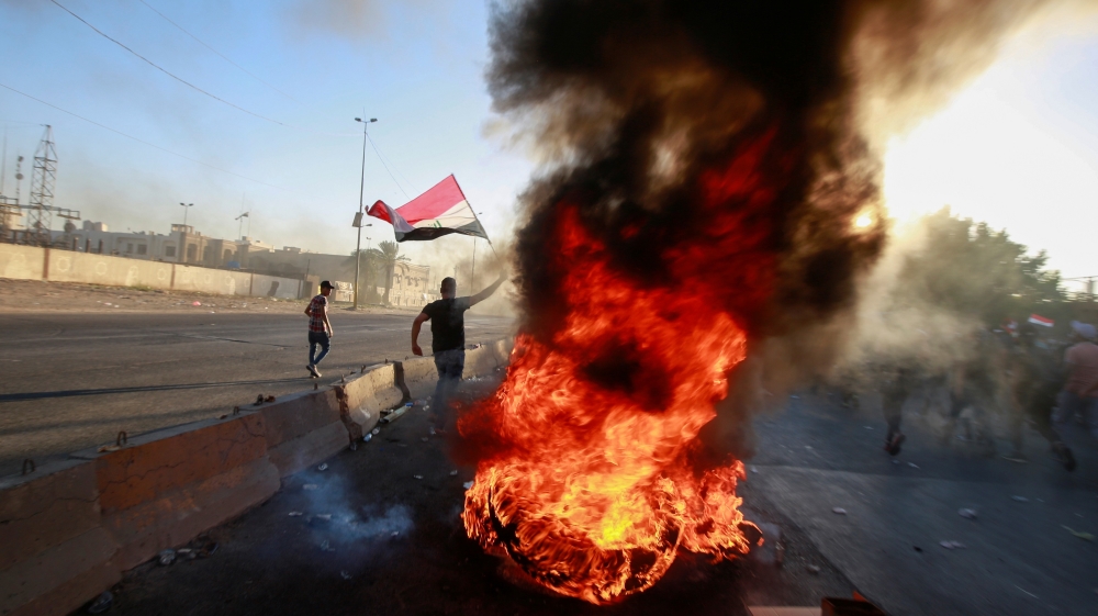 A demonstrator holds the Iraqi flag near burning objects at a protest during a curfew, three days after the nationwide anti-government protests turned violent, in Baghdad, Iraq October 4, 2019