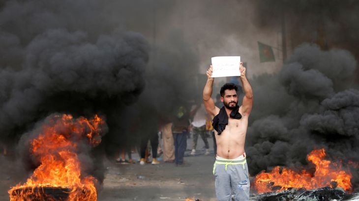 A demonstrator holds a sign as others block the road with burning tires during a protest over unemployment, corruption and poor public services, in Baghdad, Iraq October 2, 2019. REUTERS/Wissm al-Okil