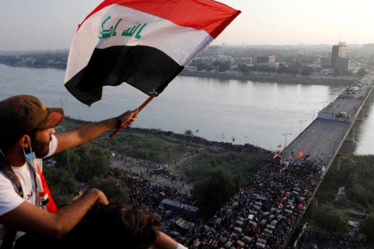 A demonstrator holds an Iraqi flag as he sits on a building during an anti-government protests in Baghdad, Iraq October 30, 2019.