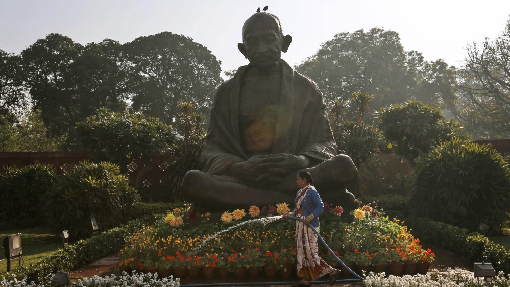 A worker waters plants around a statue of Mahatma Gandhi inside the premises of Parliament as Indian Finance Minister Palaniappan Chidambaram delivers the annual budget in New Delhi, India, Thursday, 