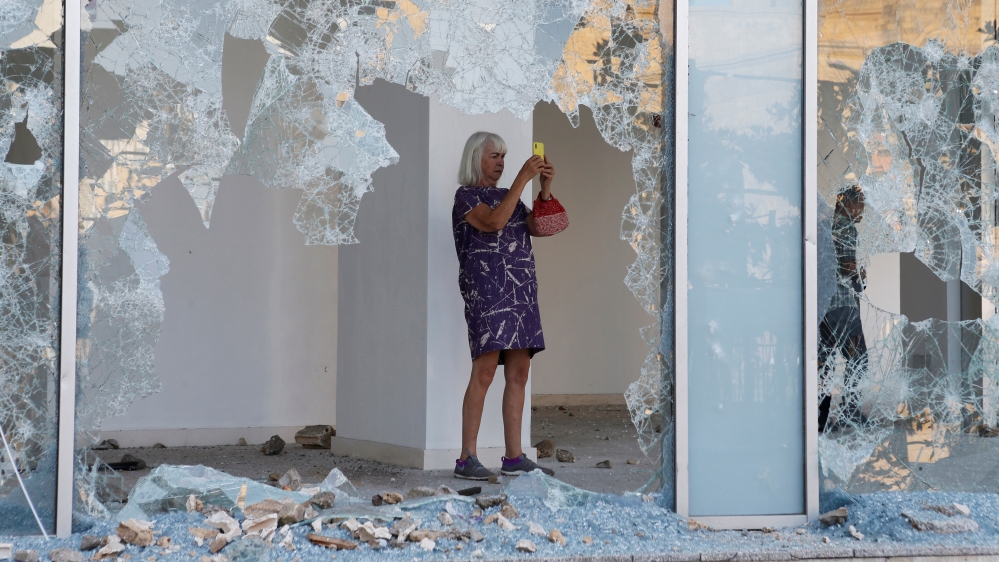 A woman takes pictures as seen through the shattered glass of a damaged shop in Beirut