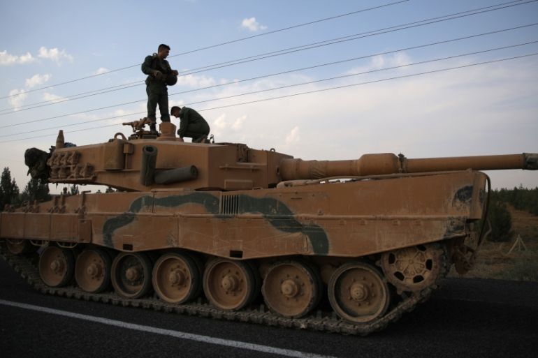 Turkish soldiers stand atop of a tank as army vehicles are moving on a road near the Turkish border town of Ceylanpinar