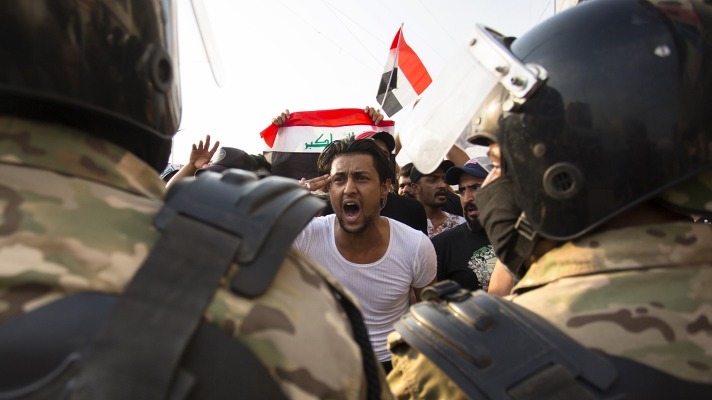 An Iraqi protestor gestures in front of security forces 