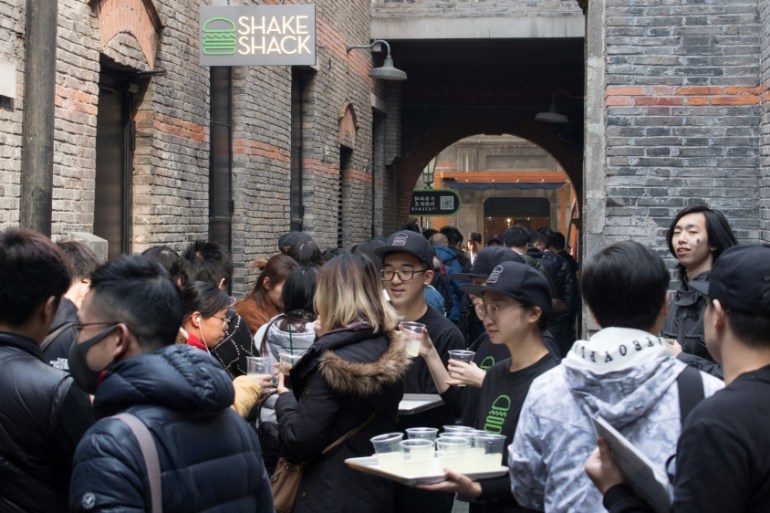 Staff members give out drinks to customers who are queuing for the newly opened U.S. burger chain Shake Shack restaurant in Shanghai