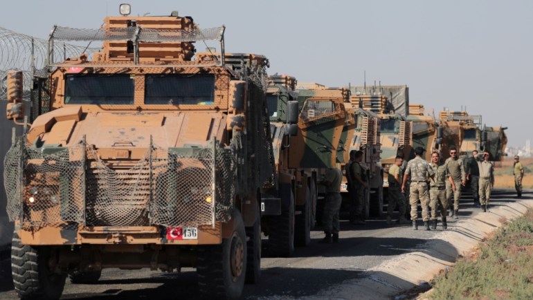 Turkish soldiers stand near military trucks in the village of Yabisa, near the Turkish-Syrian border, Syria