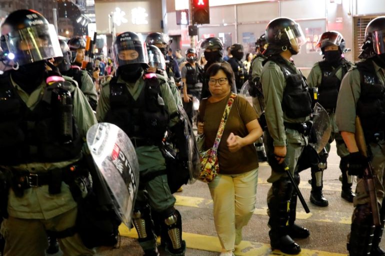 A woman makes her way between riot police as they disperse pro-democracy demonstrators gathering to commemorate the three-month anniversary of an assault by more than