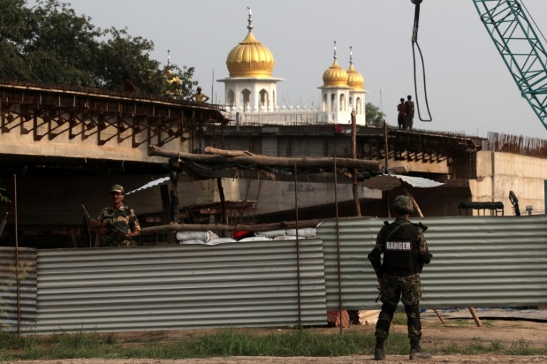 Pakistan''s paramilitary soldier and Indian soldier stand guard across steel sheets at the construction site of a bridge leading in Kartarpur