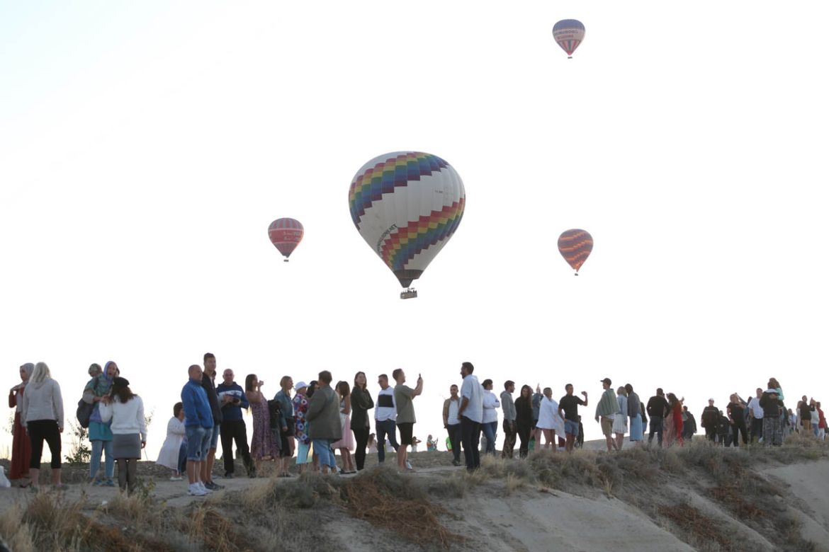 Tourists take photos as hot air balloons glide over Goreme district during early morning at the historical Cappadocia region, located in Central Anatolia''s Nevsehir province, Turkey on September 30, 2