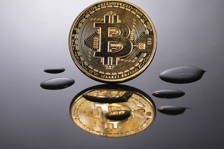 A coin representing Bitcoin cryptocurrency is reflected on a polished surface as it sits in a pool of translucent liquid in the U.K