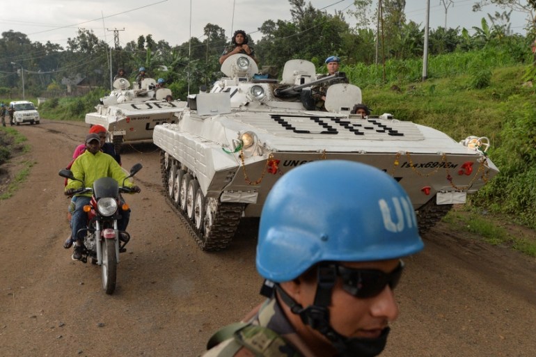 Congolese men ride on a motorcycle past peacekeepers from India, serving in the United Nations Organization Stabilization Mission in the Democratic Republic of the Congo (MONUSCO), as they drive on pa