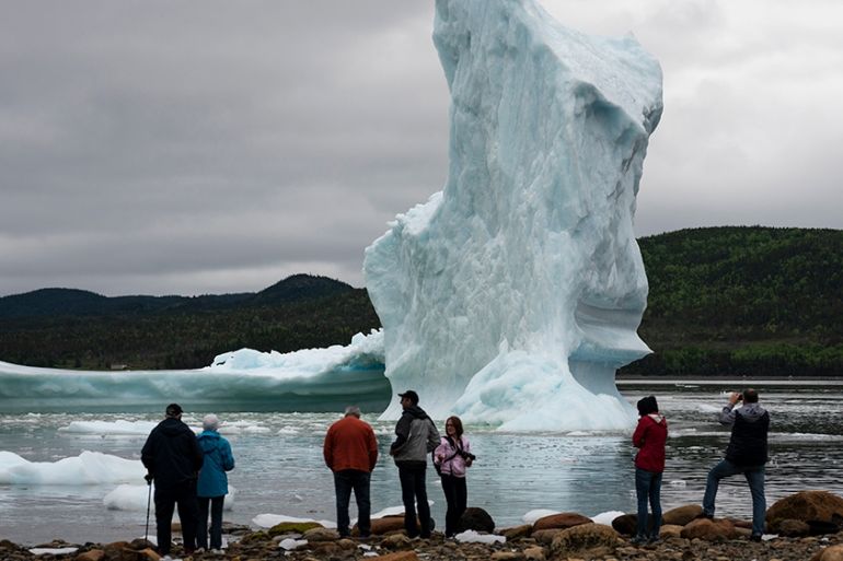 (FILES) In this file photo taken on July 3, 2019, tourists look at an iceberg from the seashore of King''s Point in Newfoundland, Canada. - The world must slash its emissions of planet-warming greenhou