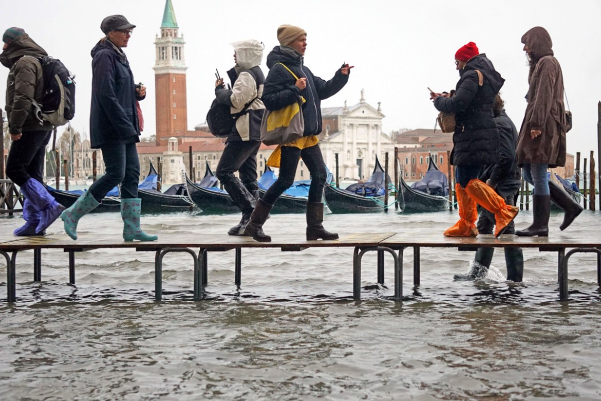 epa07990702 People walk on benches through floodwaters in Venice, Italy, 12 November 2019. The high tide has already reached the level of 1 meter above sea level in Venice at 8 am. EPA-EFE/ANDREA MER