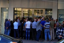 A man takes a picture with his mobile phone as people queue outside a branch of Blom Bank in Sidon