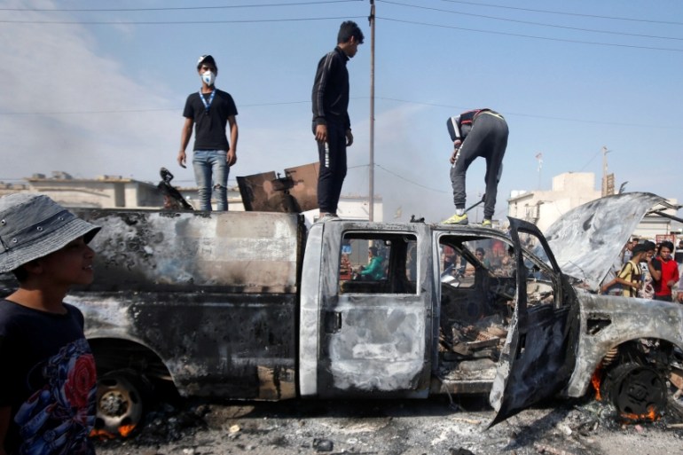 Protesters step on a military vehicle of Iraqi security forces after burning it, during ongoing anti-government protests in Basra
