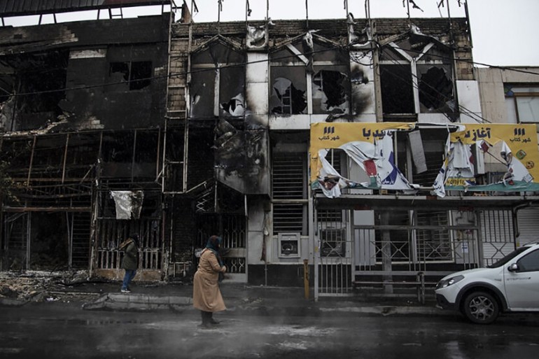 People walk past buildings which burned during protests that followed the authorities'' decision to raise gasoline prices, in the city of Karaj, west of the capital Tehran, Iran. An article published T