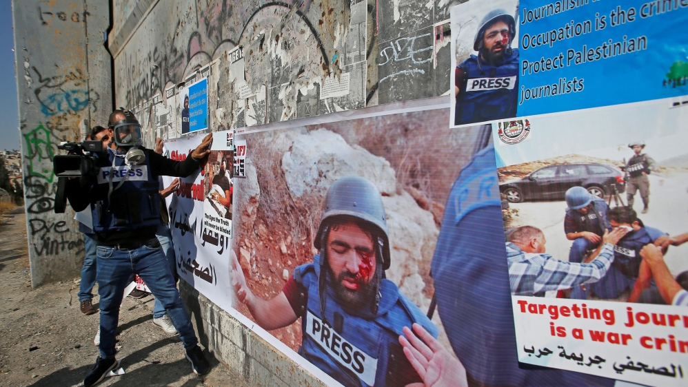 Palestinian journalists put on an Israeli gate posters showing their colleague Muath Amarna, who was shot in his eye, during a protest to show solidarity with him