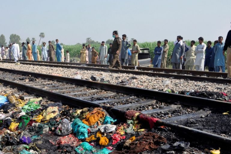 People gather near a track with the charred belongings of passenger victims, after a fire broke out in a passenger train and destroyed three carriages near the town of Rahim Yar Khan, Pakistan
