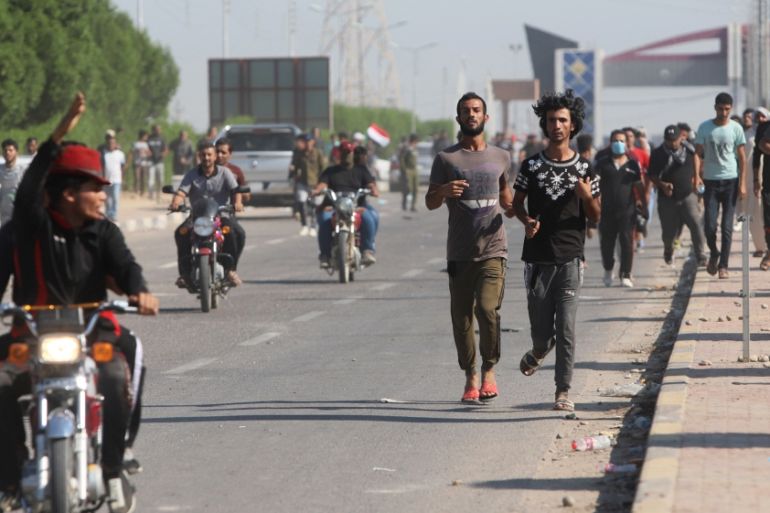 Iraqi demonstrators run away during clashes with Iraqi army forces, guard at the entrance of Umm Qasr Port during ongoing anti-government protests, south of Basra
