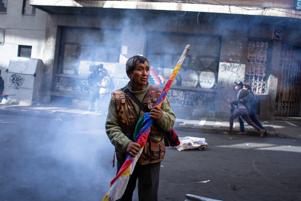 A man stands with the Wiphala, the indigenous flag, amid the tear gas during a demonstration that turned violent in support of the ousted president Evo Morales La Paz, Bolivia. Nov. 15, 2019 © Erika P