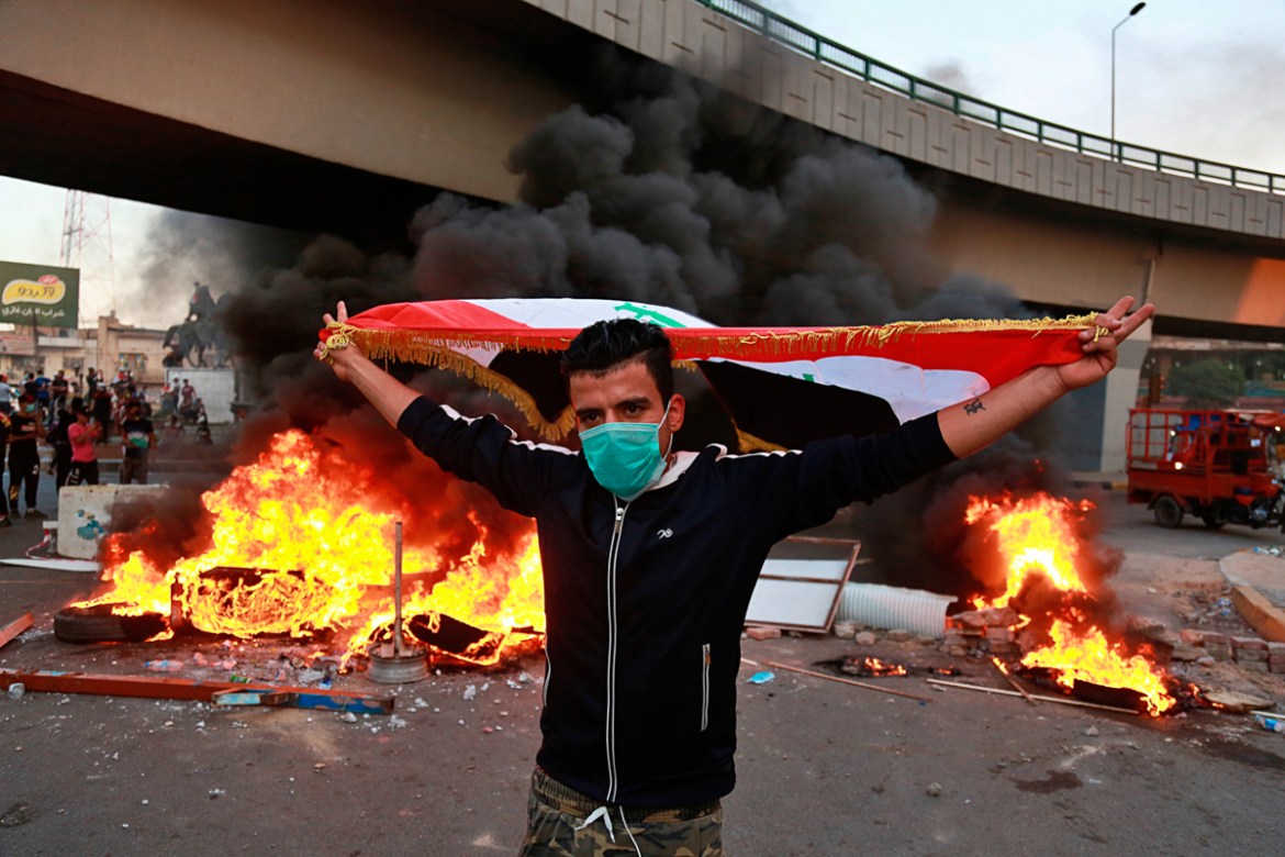 A protester holds an Iraqi flag while anti-government protests set fire while security forces fired live ammunition and tear gas near the state-run TV in Baghdad, Iraq, Monday, Nov. 4, 2019. (AP Photo