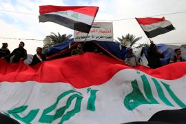 Iraqi demonstrators carry Iraqi flags during ongoing anti-government protests, in Baghdad