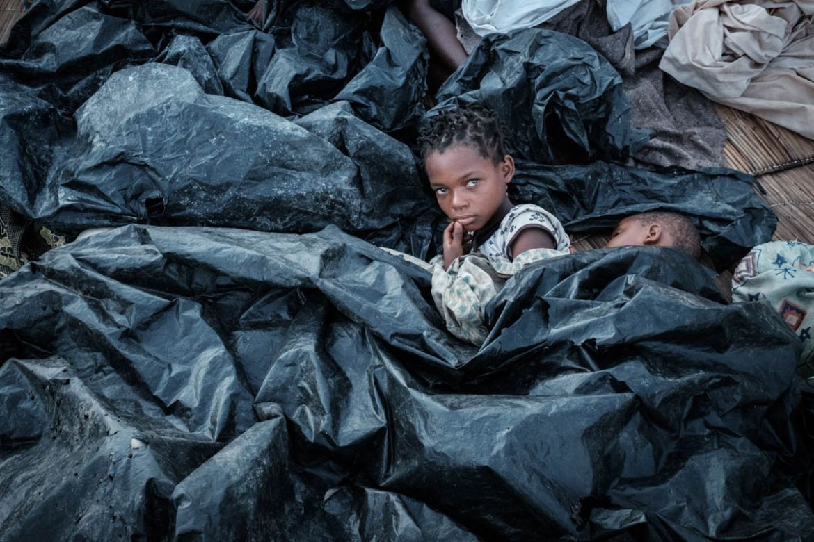 Enia Joaquin Luis, 11, wakes up beside her sister Luisa, 6, under plastic sheets for protect themselves from rain as they stay in shelter at the stands of Ring ground in Buzi, Mozambique, on March 23,