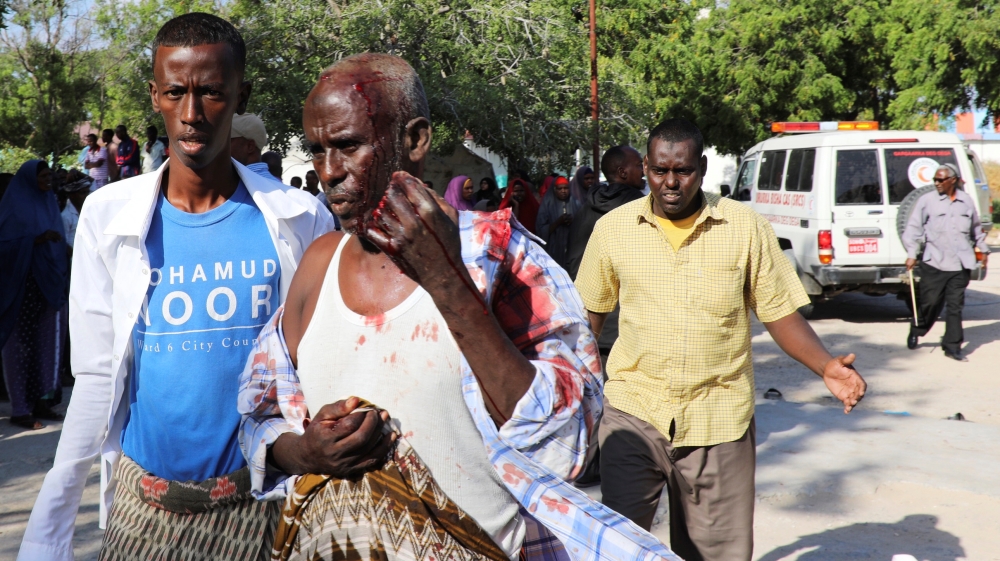 A man assists a civilian injured at the scene of a car bomb explosion at a checkpoint in Mogadishu