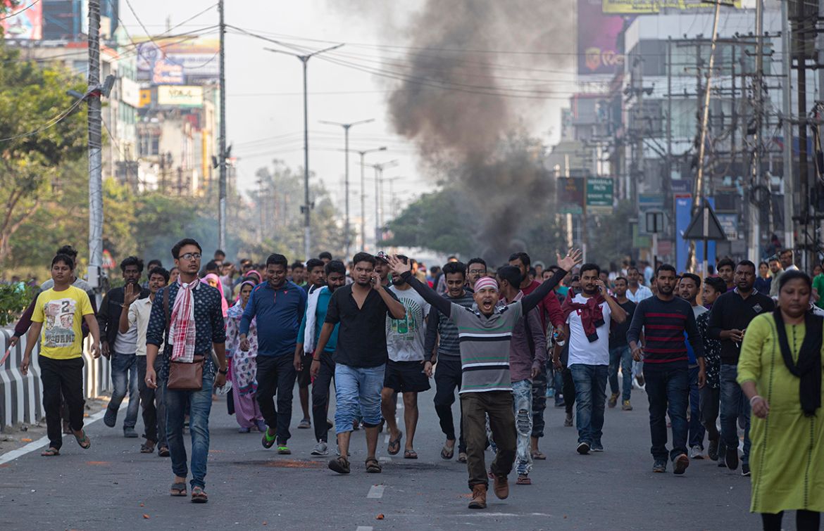 Smoke emits from burning tires as protestors walk defying a curfew in Gauhati, India, Thursday, Dec. 12, 2019. Police arrested dozens of people and enforced curfew on Thursday in several districts in