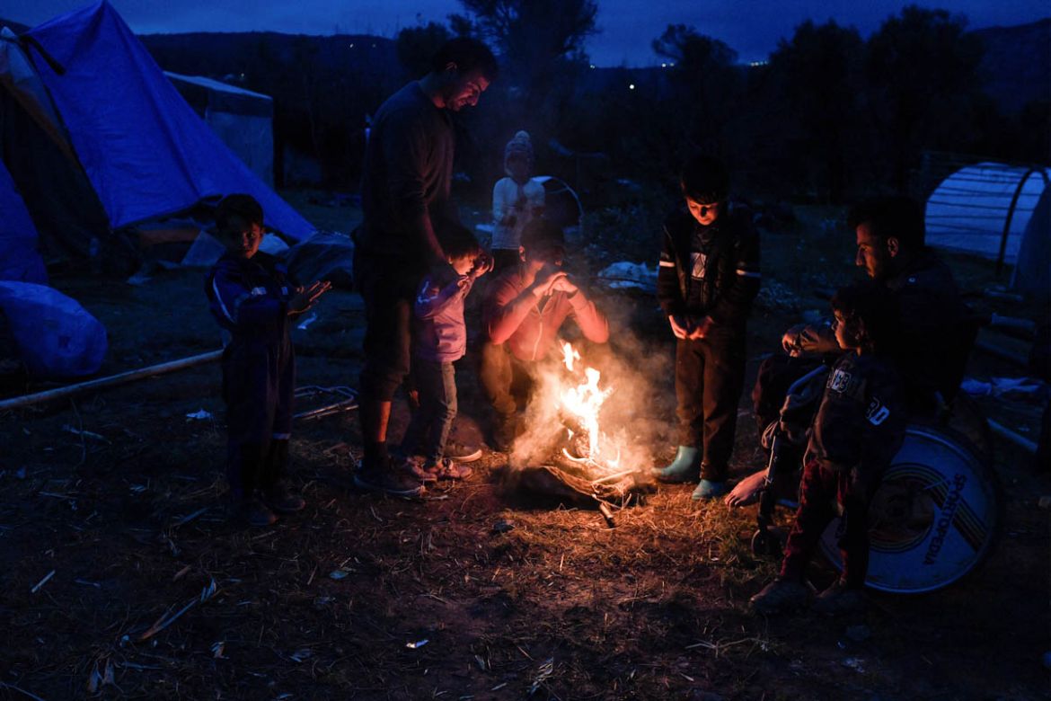 Syrian Kurds warm by a fire in the overcrowded makeshift migrant camp on the island of Chios on December 10, 2019. Thousands of refugees and migrants live in squalid condition while winter has started